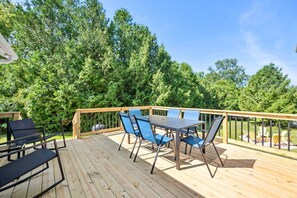 A wooden deck with a table and chairs, surrounded by lush greenery.