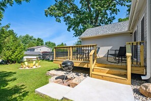 A backyard with a wooden deck, outdoor seating, and a barbecue grill.