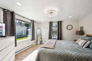 A bedroom with a bed, a dresser, a mirror, a clock, and a window with curtains.