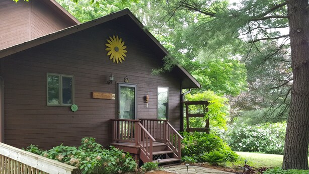 A wooden cabin with a porch, a stone pathway, and surrounding greenery. - Woodland Hideaway a Cozy & Relaxing Finger Lakes 2 bedroom home in Naples NY (Naples)