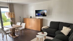 Un soggiorno moderno con un divano grigio scuro, un tavolo da pranzo in legno con sedie, un tavolino da caffè bianco e una TV a parete.
