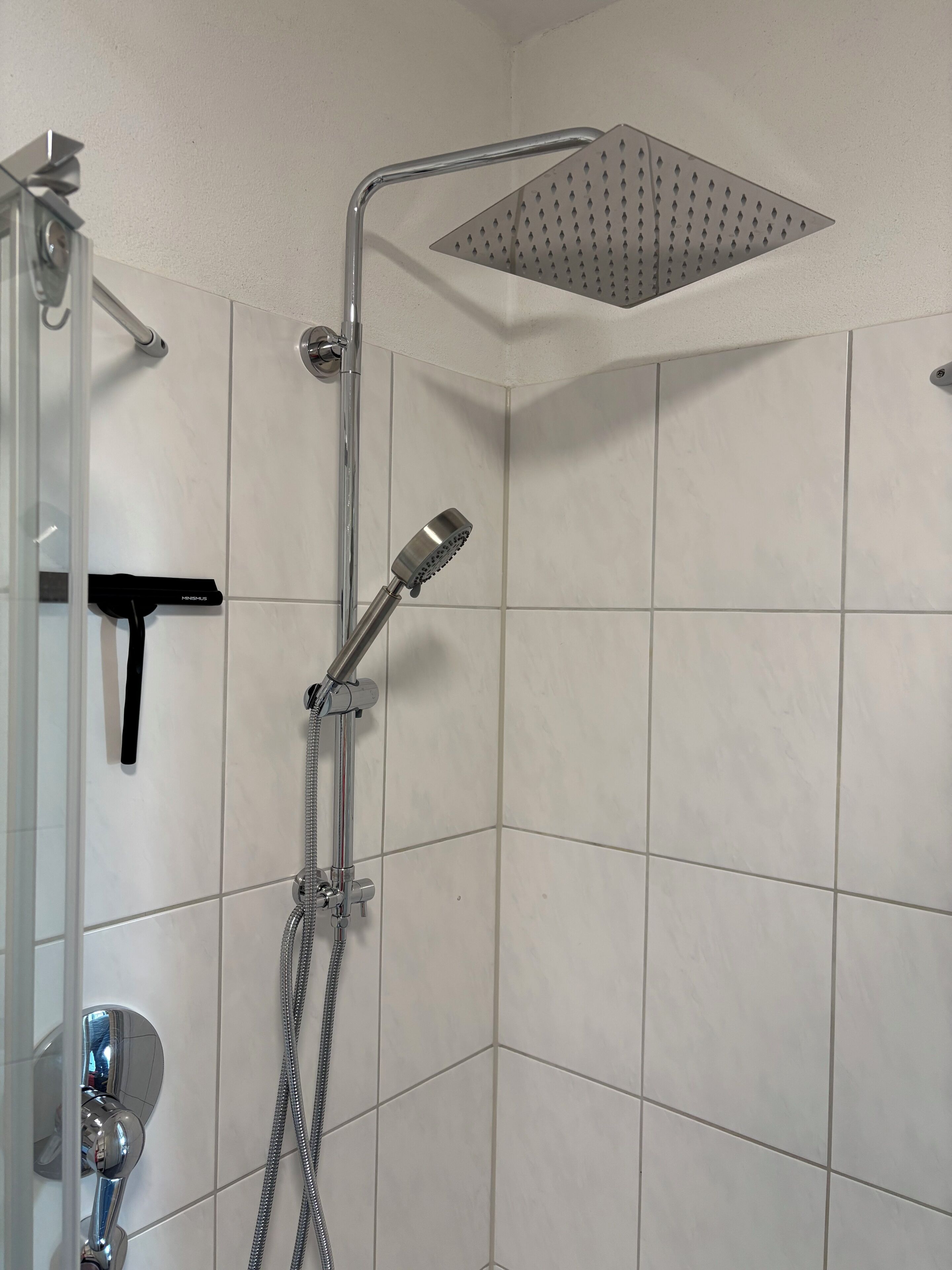 Une douche équipée d’un pommeau de douche à main et d’un pommeau de douche fixe, ainsi que d’un flexible de douche et d’un panneau de commande.