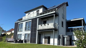 A modern two-story house with a balcony, large windows, and a well-maintained lawn. - Cozy vacation apartment with sun terrace (Schlitz)
