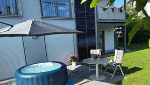 A backyard with a hot tub, a table with chairs, and a patio umbrella. - Cozy vacation apartment with sun terrace (Schlitz)