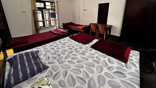 Une chambre avec deux lits simples, un bureau avec des chaises, une fenêtre avec des rideaux et un ventilateur de plafond.
