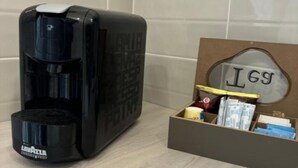 A coffee maker and a storage box with items on a tiled floor.