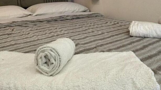 A neatly made bed with a striped bedspread and two pillows. A rolled white towel is placed on the bed.