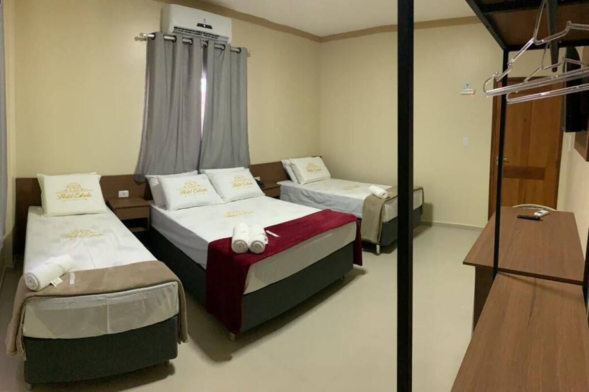 A hotel room with three single beds, a wooden wardrobe, a mirror, and a hanging clothes rack.