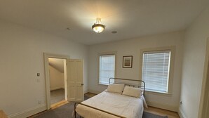 Un dormitorio con una cama, una puerta, una ventana y una lámpara en el techo.