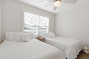 A room with two beds, a ceiling fan, and a window with blinds.