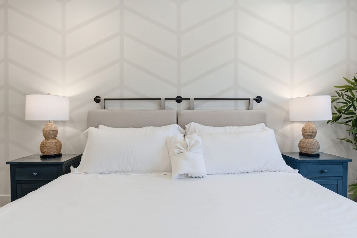 Un lit bien fait, avec du linge de lit blanc, deux tables de chevet avec des lampes et un mur orné d’un motif géométrique.