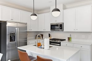 A modern kitchen with white cabinetry, stainless steel appliances, a central island, and pendant lighting.