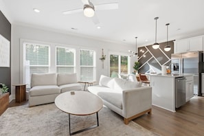 A modern living room with a sofa, coffee table, and a kitchen area with a refrigerator and island.