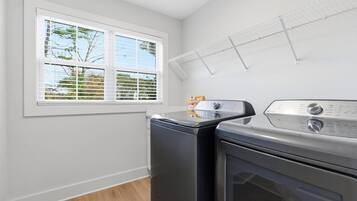 Une buanderie équipée d’un lave-linge, d’un sèche-linge et d’une fenêtre avec des stores.