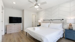 Et moderne soveværelse med seng, fjernsyn, loftventilator og et natbord med lampe.