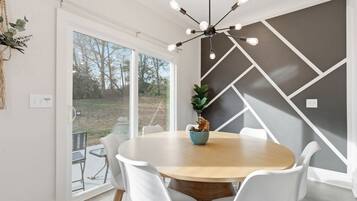 Un espace repas avec une table ronde, des chaises blanches, un lustre moderne et une vue dégagée grâce à de grandes fenêtres.