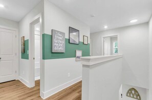 A hallway with white walls, a green accent wall, and a white door at the end.