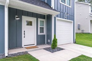 A residential house with a white garage door, a front door with a window, and a small tree in the front yard.