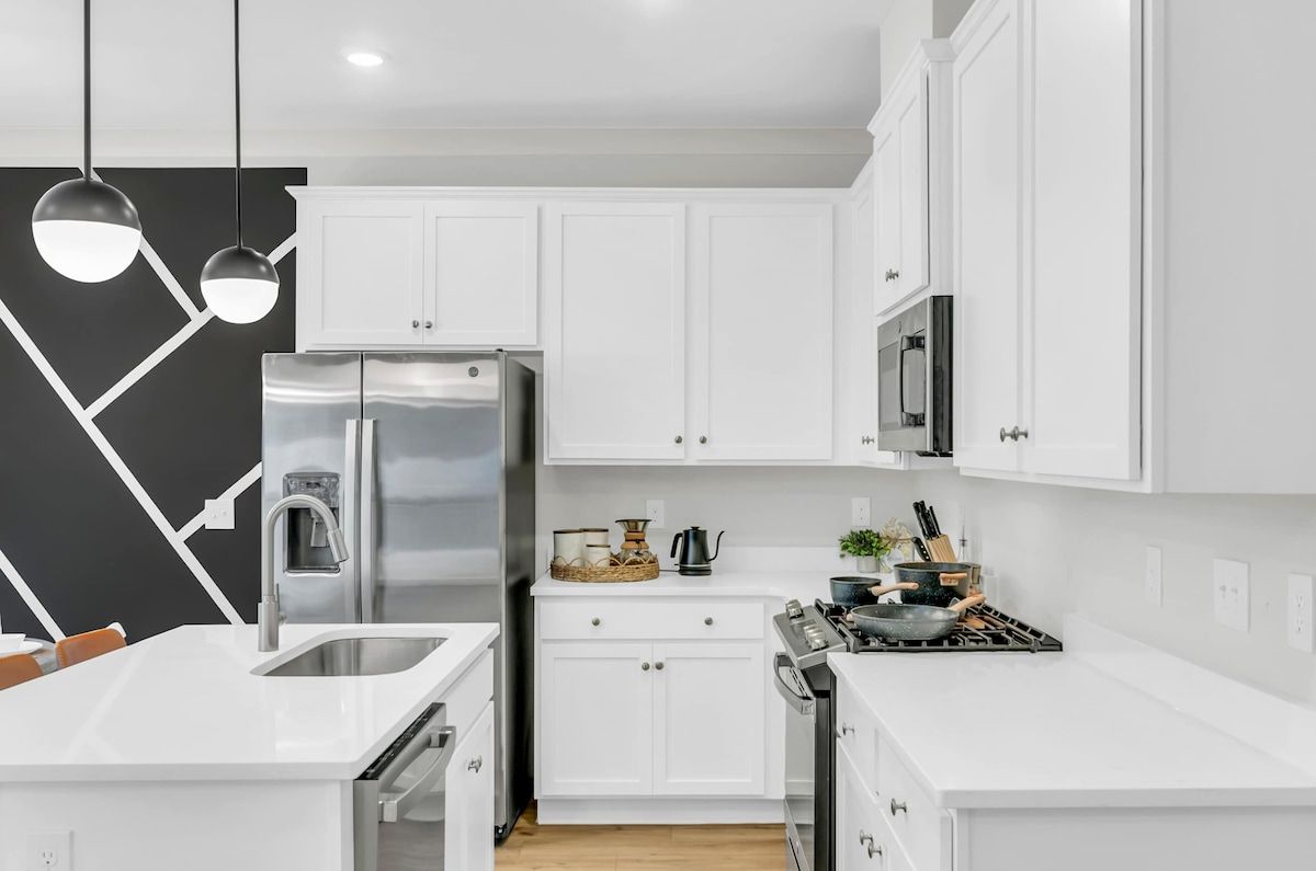 Una cocina moderna con armarios blancos, electrodomésticos de acero inoxidable e iluminación colgante.