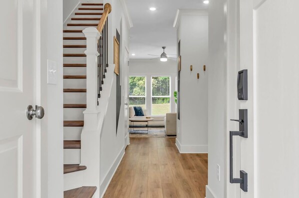 A hallway with a wooden staircase, a ceiling fan, and a view of the outdoors through a window.