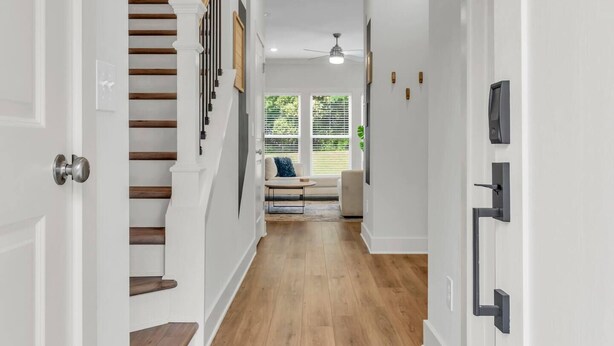 A hallway with a wooden staircase, white walls, and a ceiling fan.
