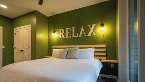 Une chambre à coucher avec un lit, un panneau mural sur lequel on peut lire « RELAX » et une fenêtre avec des stores.