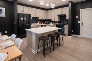 A modern kitchen with a central island, bar stools, and a dining table set for four.