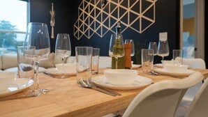 Une table à manger dressée avec de l’argenterie blanche, des verres transparents et des couverts, sur fond d’un motif géométrique mural.