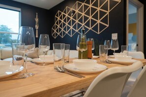 A dining table set with white plates, clear glasses, and cutlery, with a geometric wall design in the background.