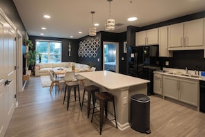 A modern kitchen with a central island, bar stools, and a dining area with a sofa and table.