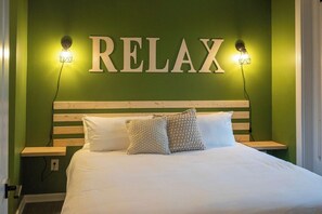 A bed with a wooden headboard, two bedside lamps, and a wall with the word 'RELAX' illuminated.