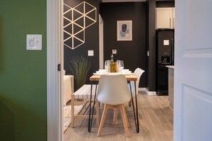 A dining area with a table set for two, a chair, a plant, and a geometric wall decoration. - Luxe Modern Loft, Great for Long Stays W/King Beds (Spartanburg)
