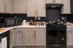 A kitchen with white cabinets, a microwave, a stove, and various cooking utensils. - Luxe Modern Loft, Great for Long Stays W/King Beds (Spartanburg)