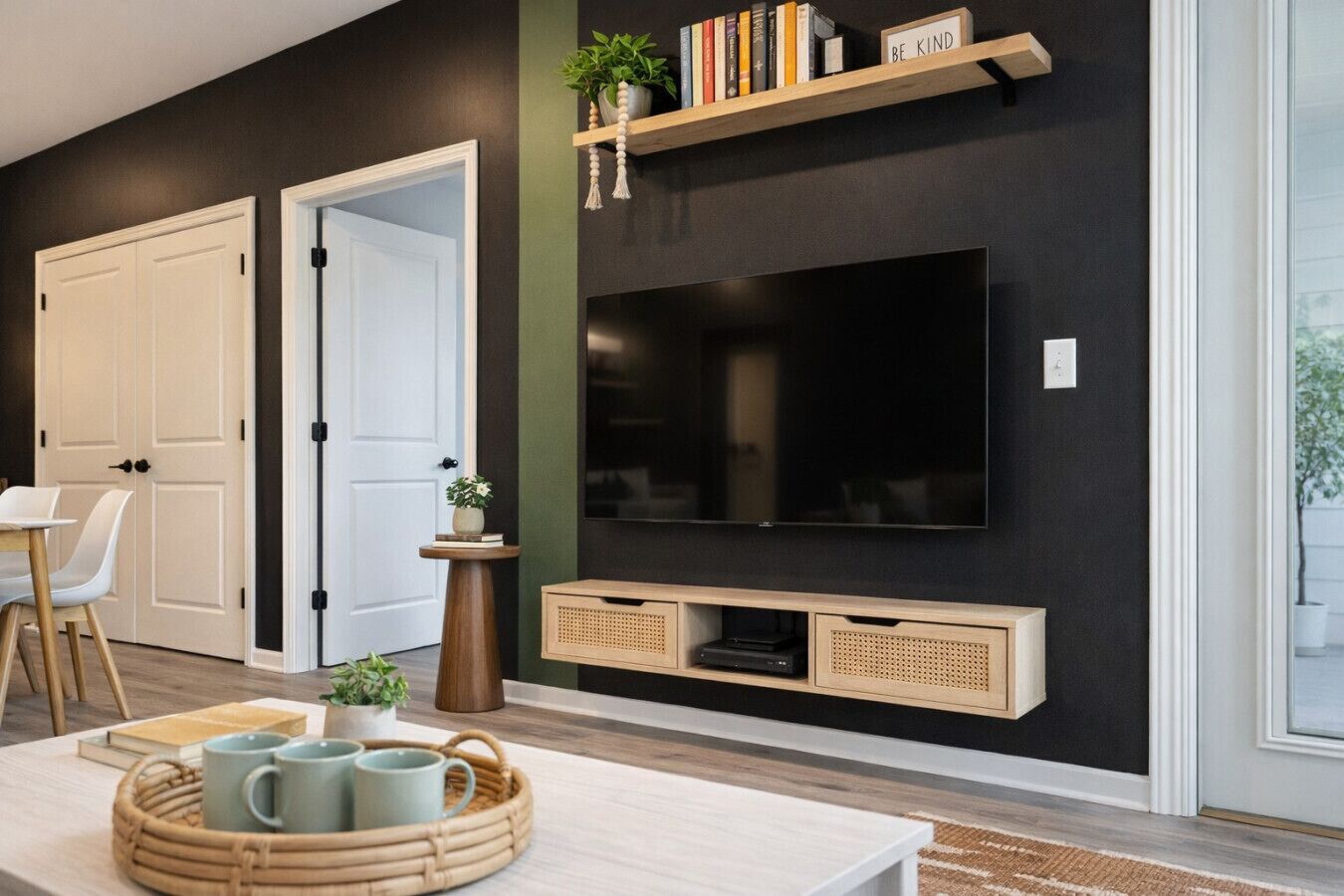 Un salon moderne avec un grand téléviseur à écran plat fixé sur un mur foncé, des étagères en bois au-dessus et une petite table d’appoint avec une plante.