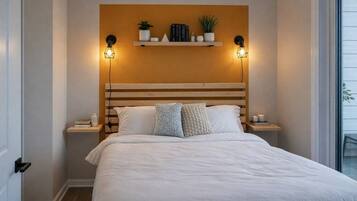 Ein Schlafzimmer mit einem großen Bett, zwei Nachttischen, einem Regal mit Büchern und Pflanzen sowie Wandleuchten.