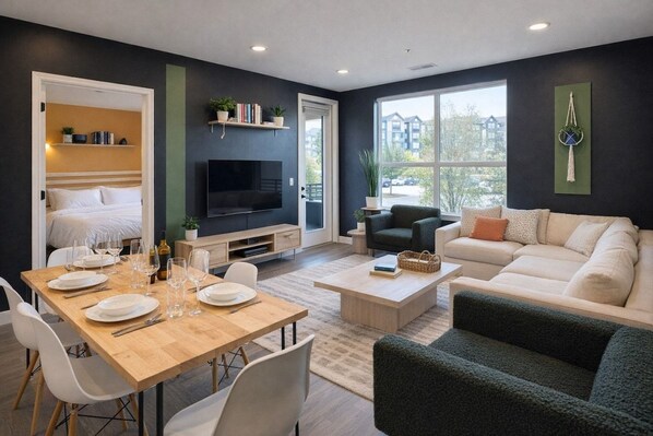 A modern living room with a dining area, a sofa set, a flat-screen TV, and a large window offering a view of the outside. - Amazing location, 2 King beds, Modern loft (Spartanburg)