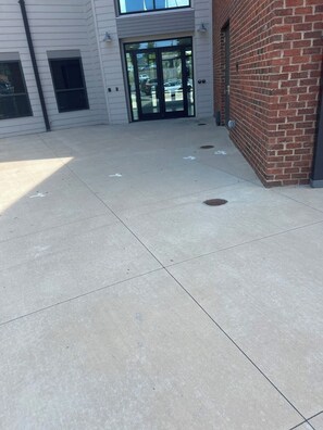 A paved courtyard with a glass door entrance, a brick wall, and a building with windows. - Ideal for long stays, great location, King bed! (Spartanburg)