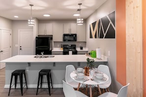 A modern kitchen with white cabinetry, a central island, and a dining area with white chairs and a table set for four. - Ideal for long stays, great location, King bed! (Spartanburg)