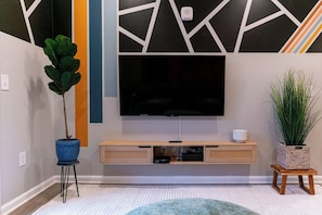 A modern living room with a flat-screen TV mounted on a wall, a wooden entertainment unit below, and two potted plants. - Ideal for long stays, great location, King bed! (Spartanburg)