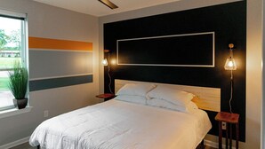 A modern bedroom with a large bed, two bedside tables, a potted plant, and a view of the outdoors. - Ideal for long stays, great location, King bed! (Spartanburg)