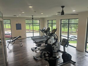 A gym with various exercise equipment, large windows, and a ceiling fan.