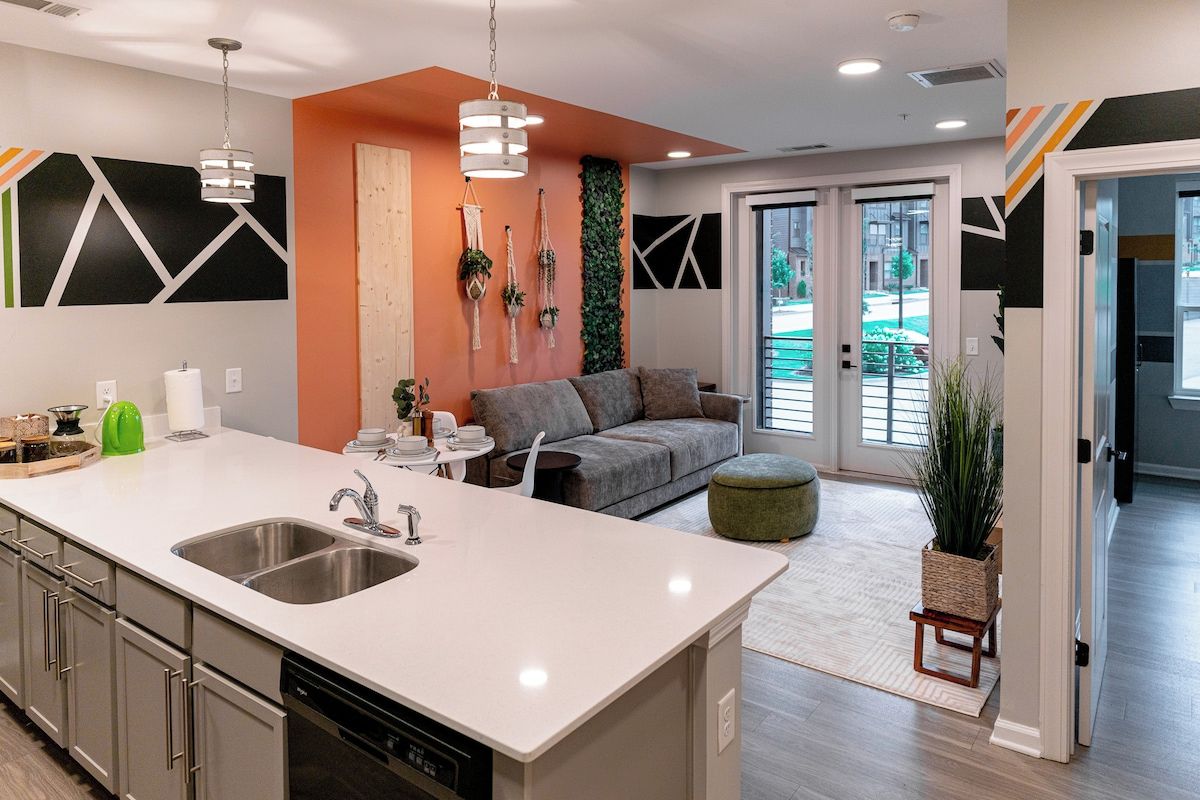 A modern kitchen with a central island, stainless steel appliances, and a seating area with a grey sofa and ottoman.