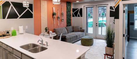 A modern kitchen with a central island, stainless steel appliances, and a seating area with a grey sofa and ottoman.