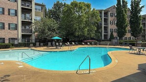 A swimming pool with lounge chairs and a small umbrella, surrounded by multi-story buildings.