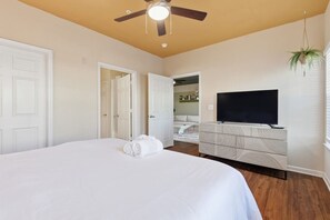 Ein Schlafzimmer mit einem Bett, einem Deckenventilator, einem Fernseher und einer Pflanze.