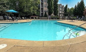 Una piscina con sillas de descanso y sombrillas, rodeada de árboles y edificios.