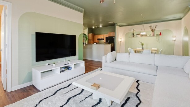 A living room with a flat-screen TV, white sofa, coffee table, and a ceiling fan.
