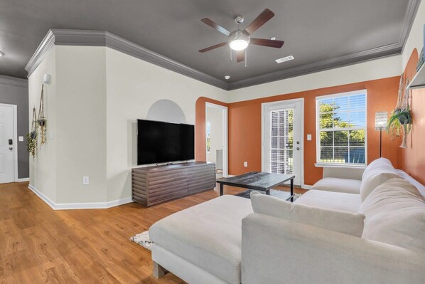 A living room with a flat-screen TV, a sofa, a coffee table, and a ceiling fan. - Pool, Gym & Central Location! 2- King Beds (Spartanburg)