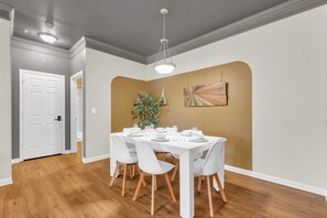 A dining area with a white table set for four, surrounded by white chairs with wooden legs. - Pool, Gym & Central Location! 2- King Beds (Spartanburg)