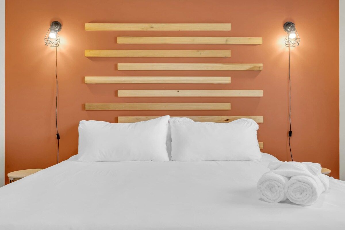 Ein Bett mit weißer Bettwäsche und zwei Kissen, ein hölzernes Kopfteil sowie zwei Wandleuchten.